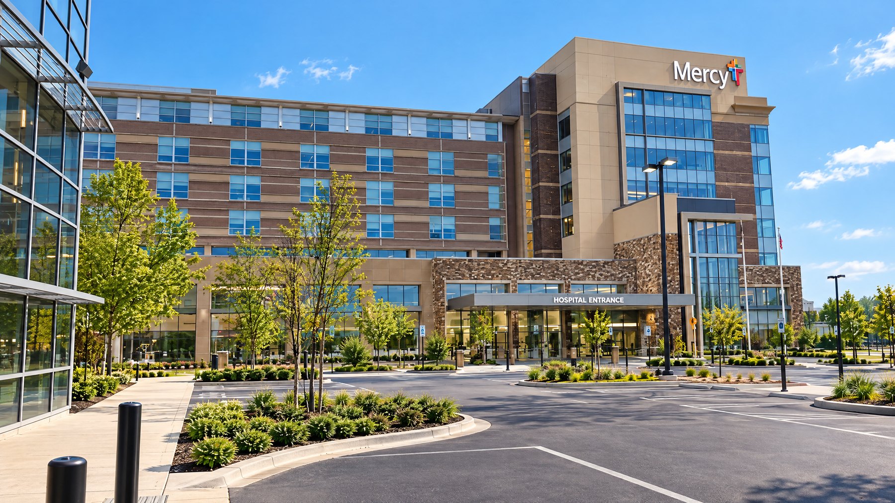A regional hospital entrance under a clear sky, glass frontage and a covered drop-off canopy, seen from the visitor parking lot
